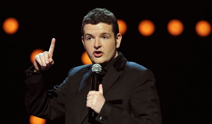 Ο Kevin Bridges στη σκηνή με μικρόφωνο, κοινό να γελάει — ανακοίνωση για Kevin Bridges Ελλάδα