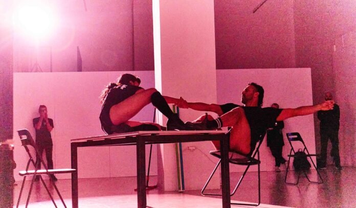 Σκηνική εικόνα από το Outliers arisandmartha έργο με δύο performers σε αντιπαράθεση και έντονο φωτισμό